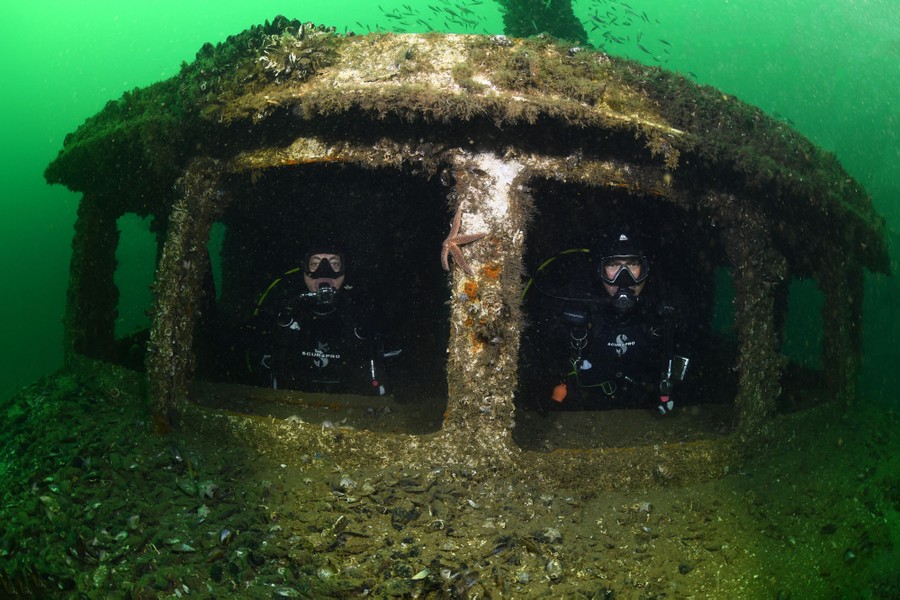 Two scuba divers pose inside the sunken wreck of a passenger ferry.