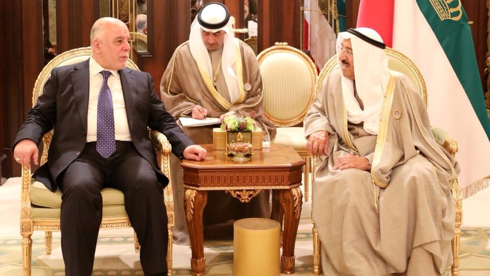 Iraq's prime minister, who is dressed in a suit, talks to the emir of Kuwait, who is dressed in traditional clothes. 