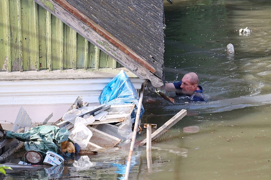 A person swims in deep floodwater beside a house.