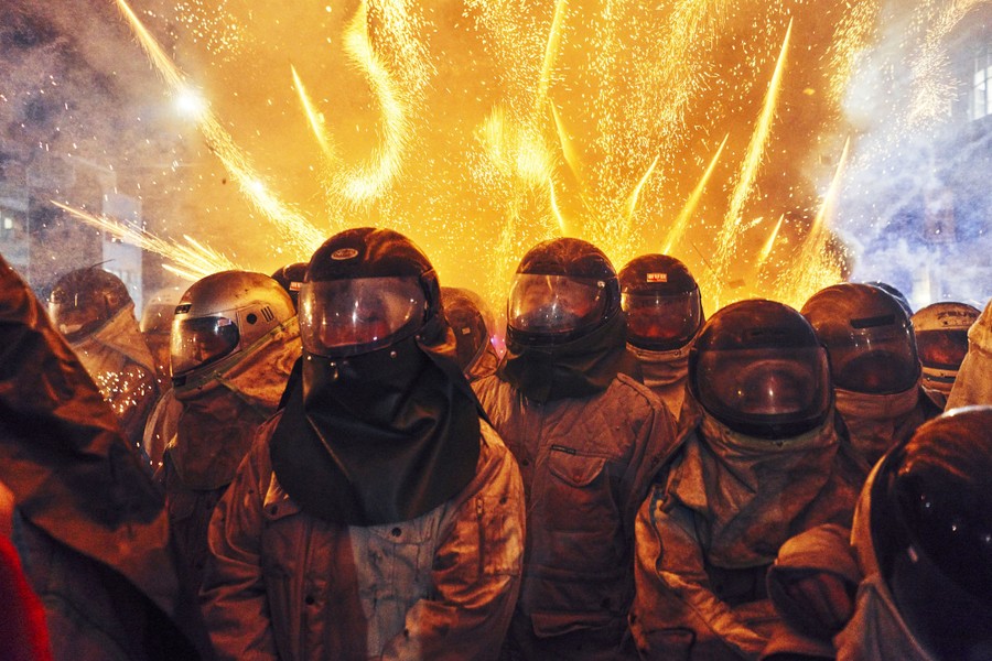 Helmeted people stand together as fireworks explode behind them.