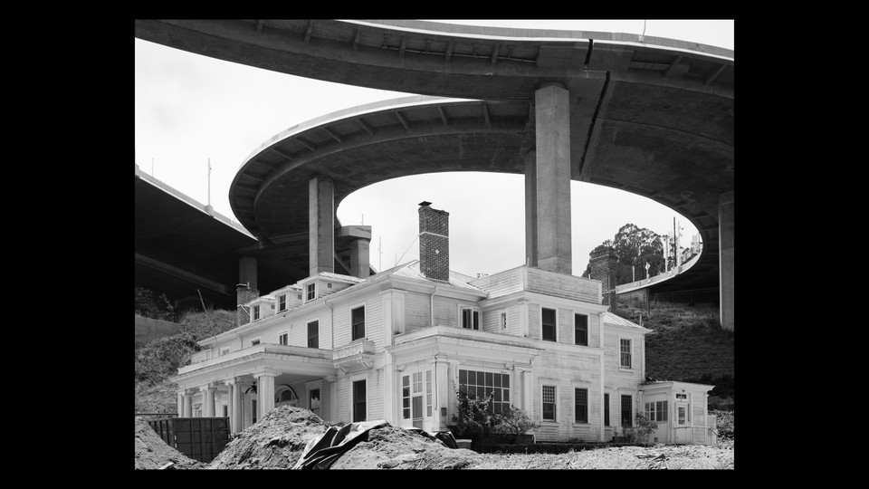 A crumbling house in the middle of a construction site and highway