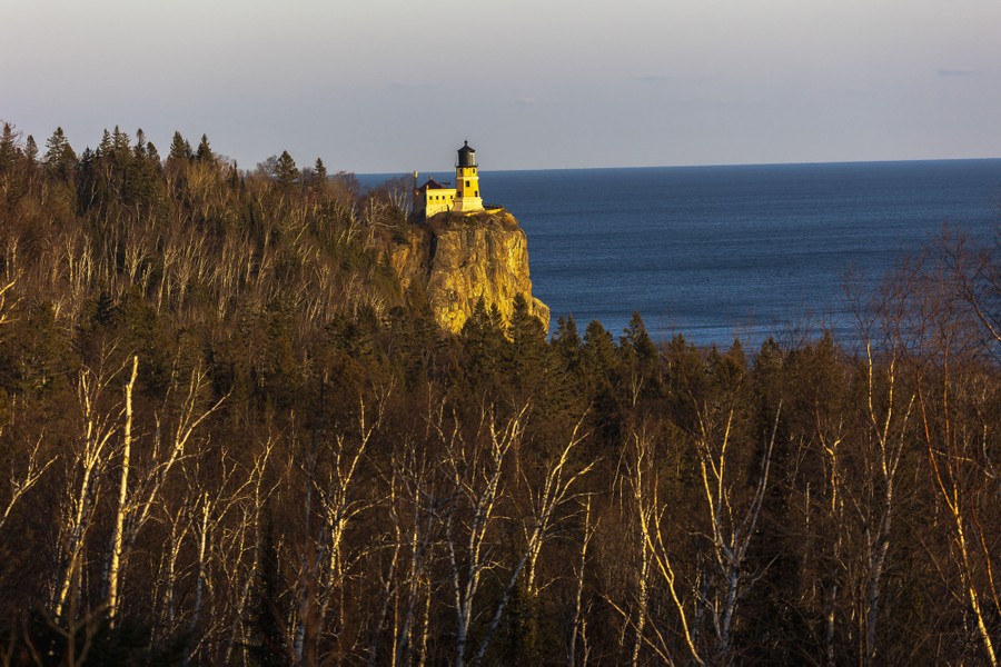 A lighthouse is seen among trees on a cliff above Lake Superior.