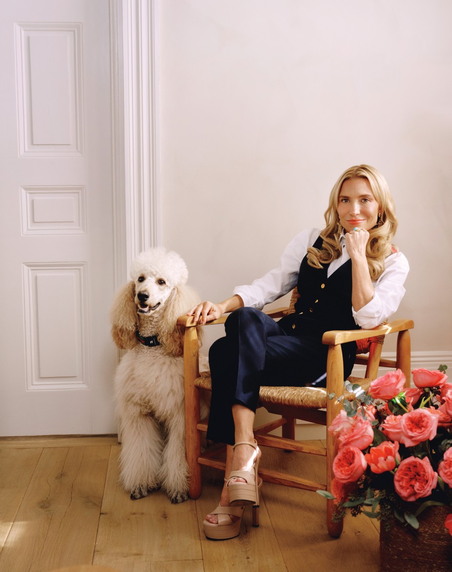photo of Andersen in white shirt with blue vest and pants, seated in chair between large poodle and large basket of pink flowers