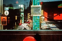 A man, photographed through a large window, reads a newspaper by himself in a restaurant.