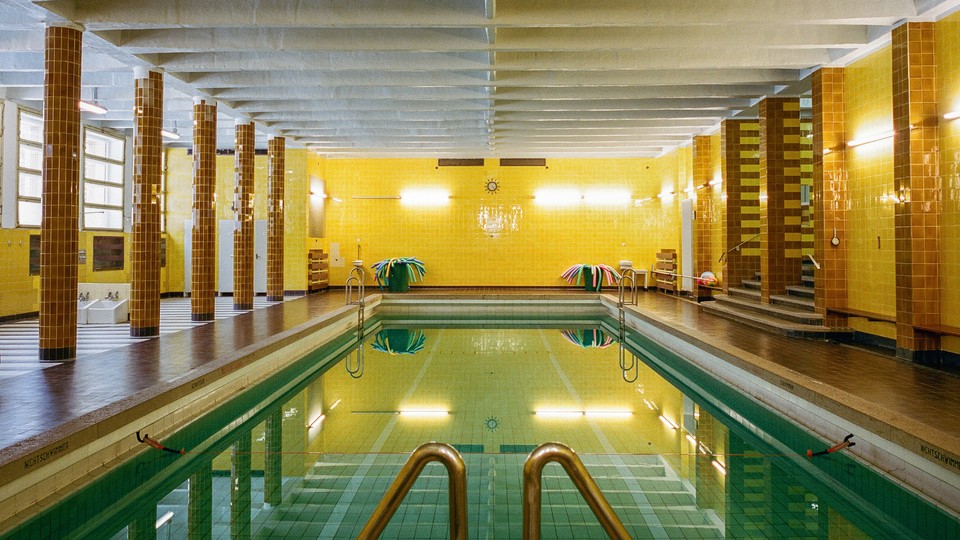 A blue swimming pool in a yellow tiled room with brown tiled columns