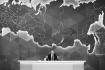 Vladimir Putin sits behind a desk and in front of a map.