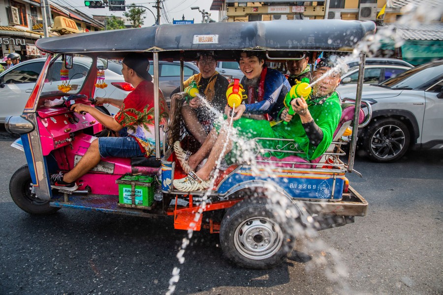 Several people in a tuk-tuk squrt water guns toward the photographer.