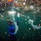 A diver floats just below the surface, surrounded by pieces of debris and plastic garbage.