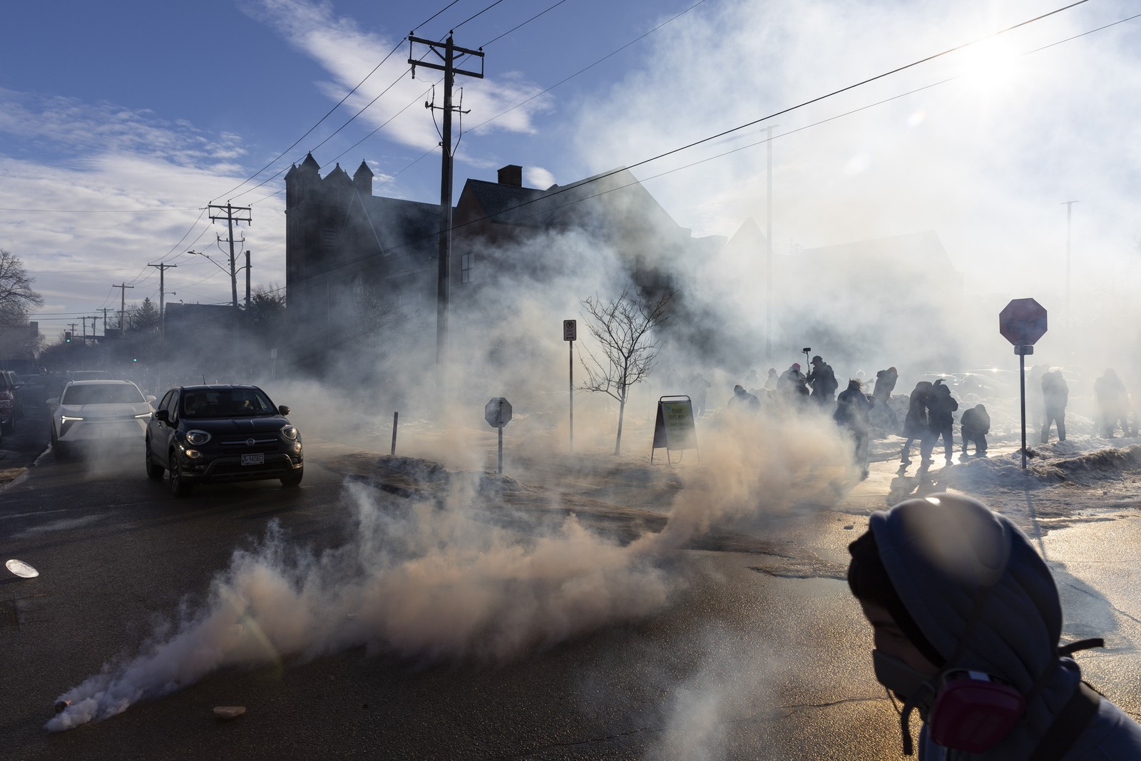 Protesters and onlookers leave as tear gas fills an intersection in a residential neighborhood.