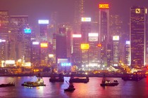 A bright city skyline illuminates fishing boats in a harbor.