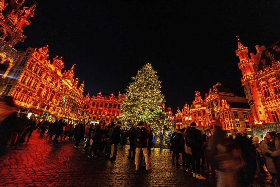 A crowd gathers in a city square among Christmas lights and decorations.
