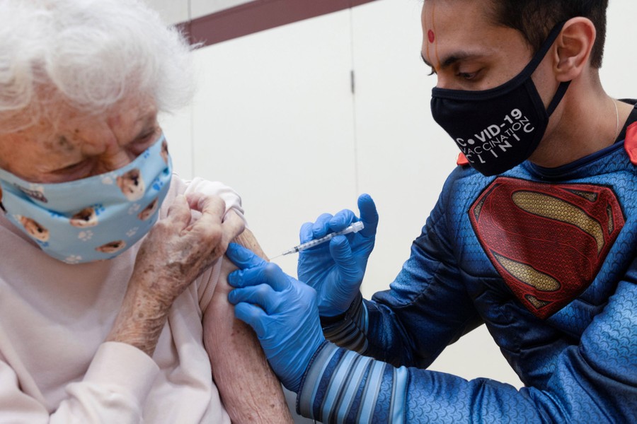 A health-care worker wearing a Superman costume injects a woman with a vaccine dose.