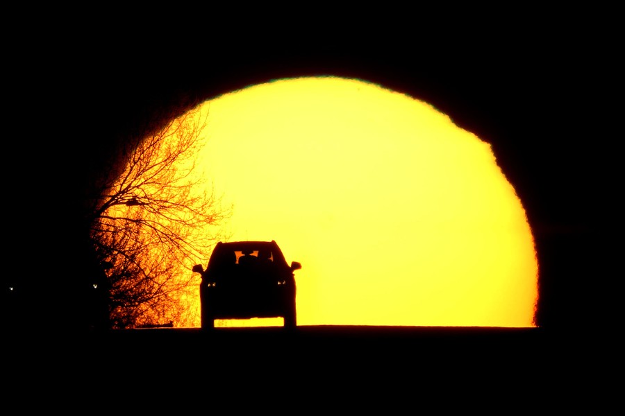 A car is silhouetted against the setting sun.