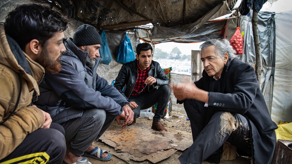 Bernard-Henri Lévy in his latest documentary, speaking to three men in a large makeshift tent