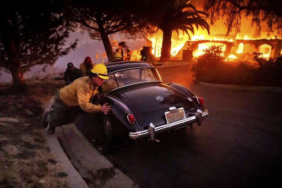 Firefighters push a vintage car away from a burning home during a wildfire.