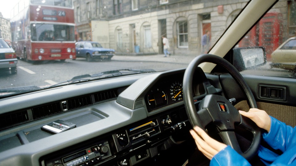 A person in their car with a double-decker bus outside