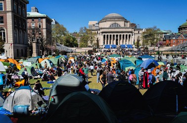 Pro-Palestinian protesters sit and stand, some in front of tents, in a large grassy area at Columbia University.