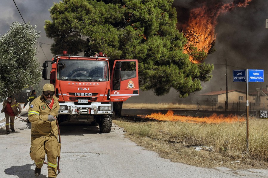 Dry grass and a tree catch fire near firefighters and a fire truck.