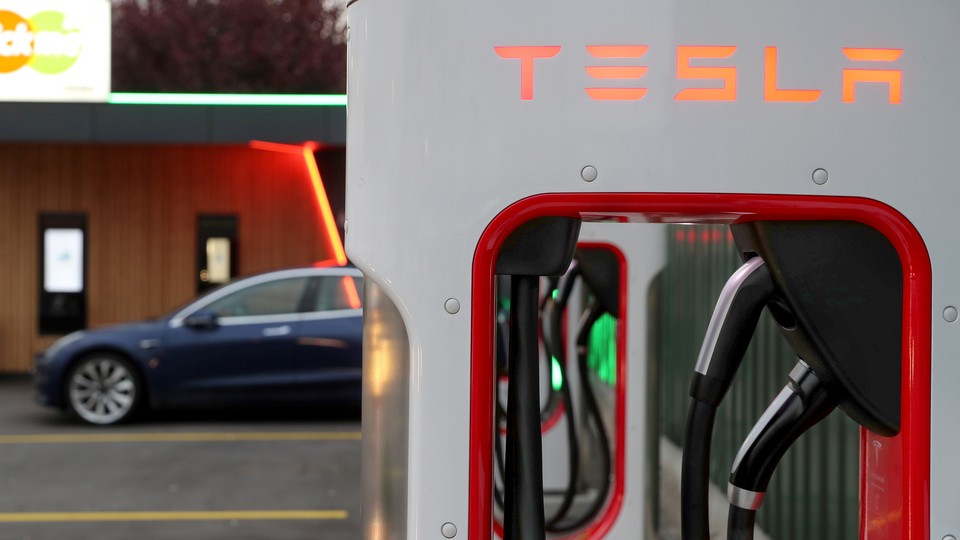 A Tesla Supercharger in the foreground, with a car in the background