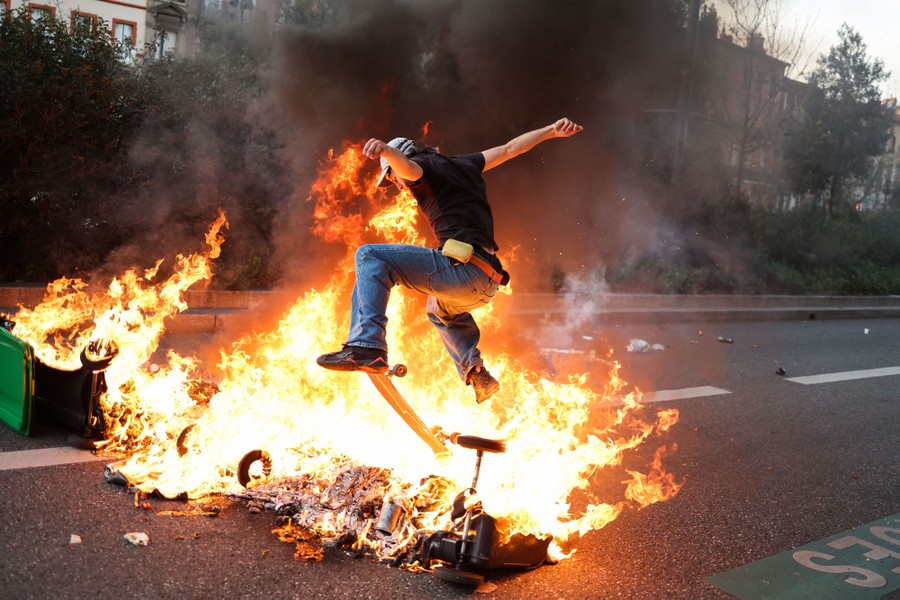 A protester jumps a skateboard over burning garbage.