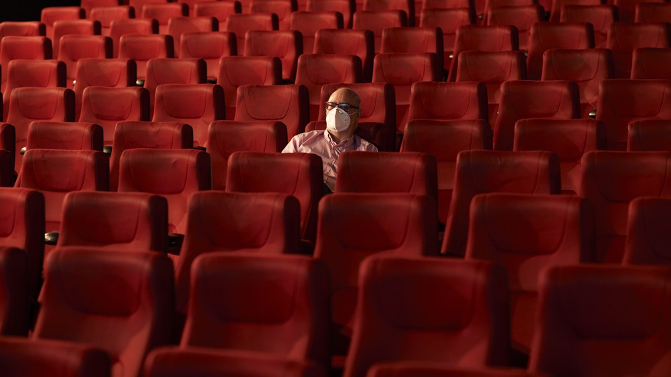 A man wearing a mask sits alone in a theater.