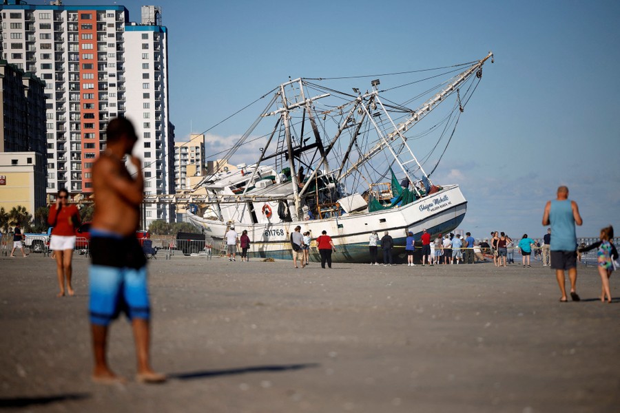 Beachgoers look at a large shrimping boat that was swept ashore by Hurricane Ian.