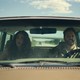 A woman and a man are in a car, with frightened looks on their faces.