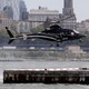 An Uber Copter lands at the Downtown Manhattan Heliport, in sight of buildings and the water.