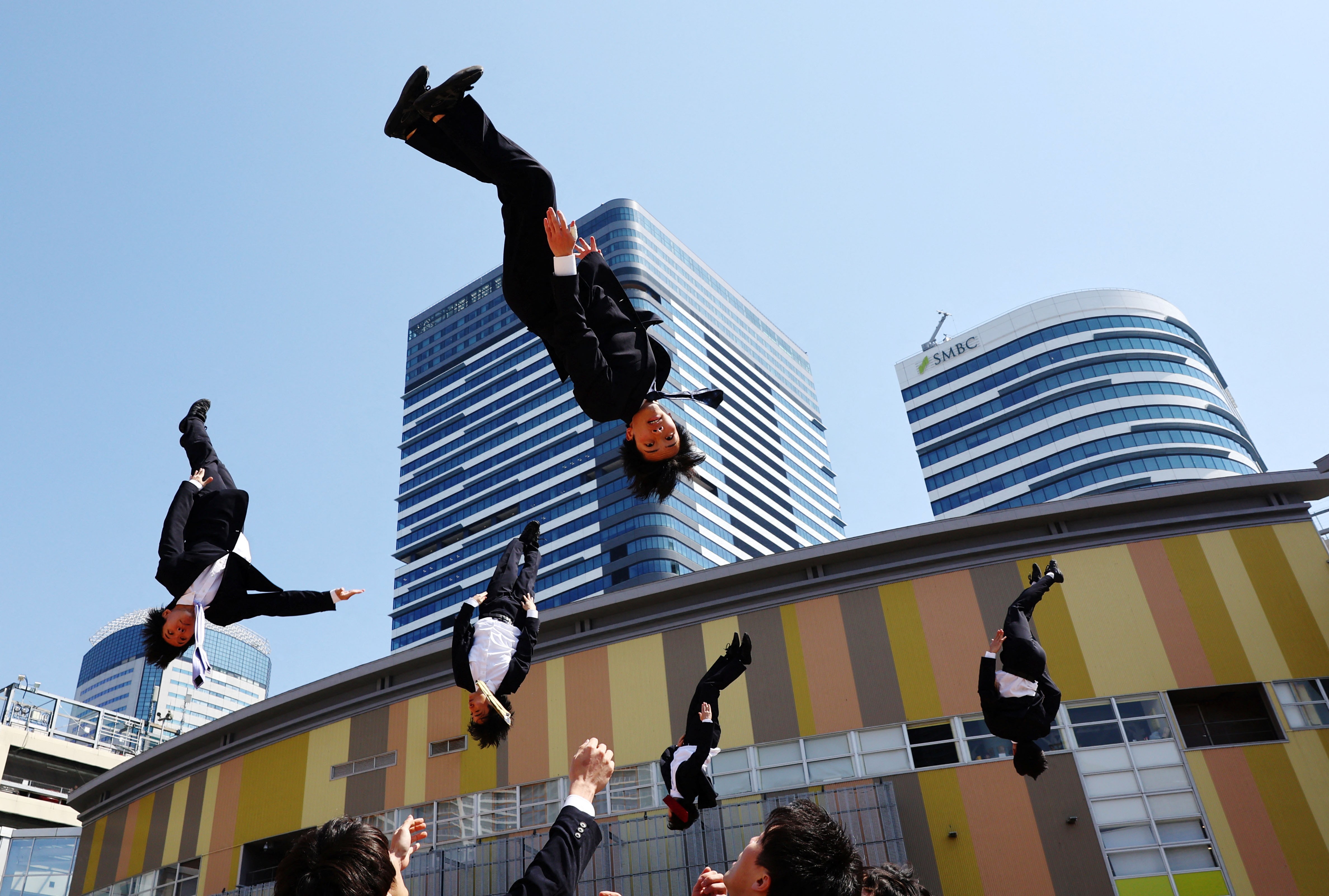 Five men in business suits are seen in mid-air during an acrobatic performance.