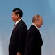 Xi Jinping and Vladimir Putin stand back to back in black suits, Xi towering over Putin.