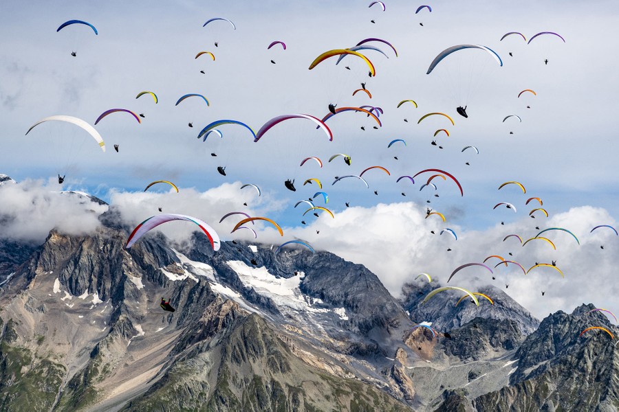 Dozens of paragliders fly in the same direction above high mountaintops.