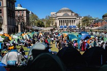 Pro-Palestinian protesters sit and stand, some in front of tents, in a large grassy area at Columbia University.