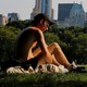 Two male figures recline on a grassy field. Manhattan's skyscrapers rise in the background.