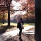 A woman walks along a sidewalk among trees in autumn.