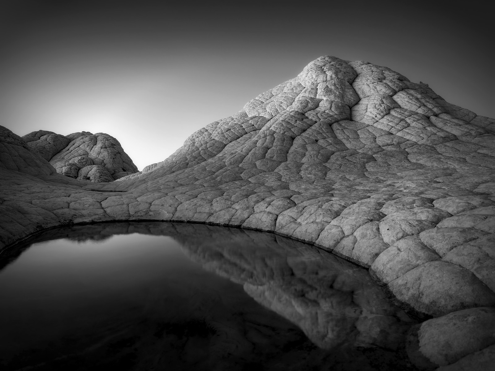 A black-and-white view of a cracked and weather-worn rock outcrop beside a small body of water