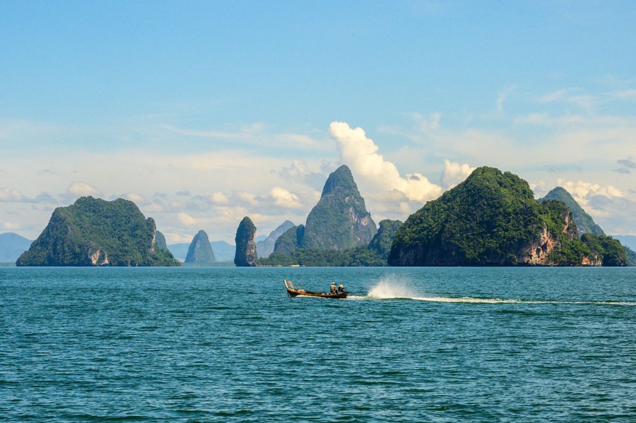 A small powerboat motors past steep islands in a bay.