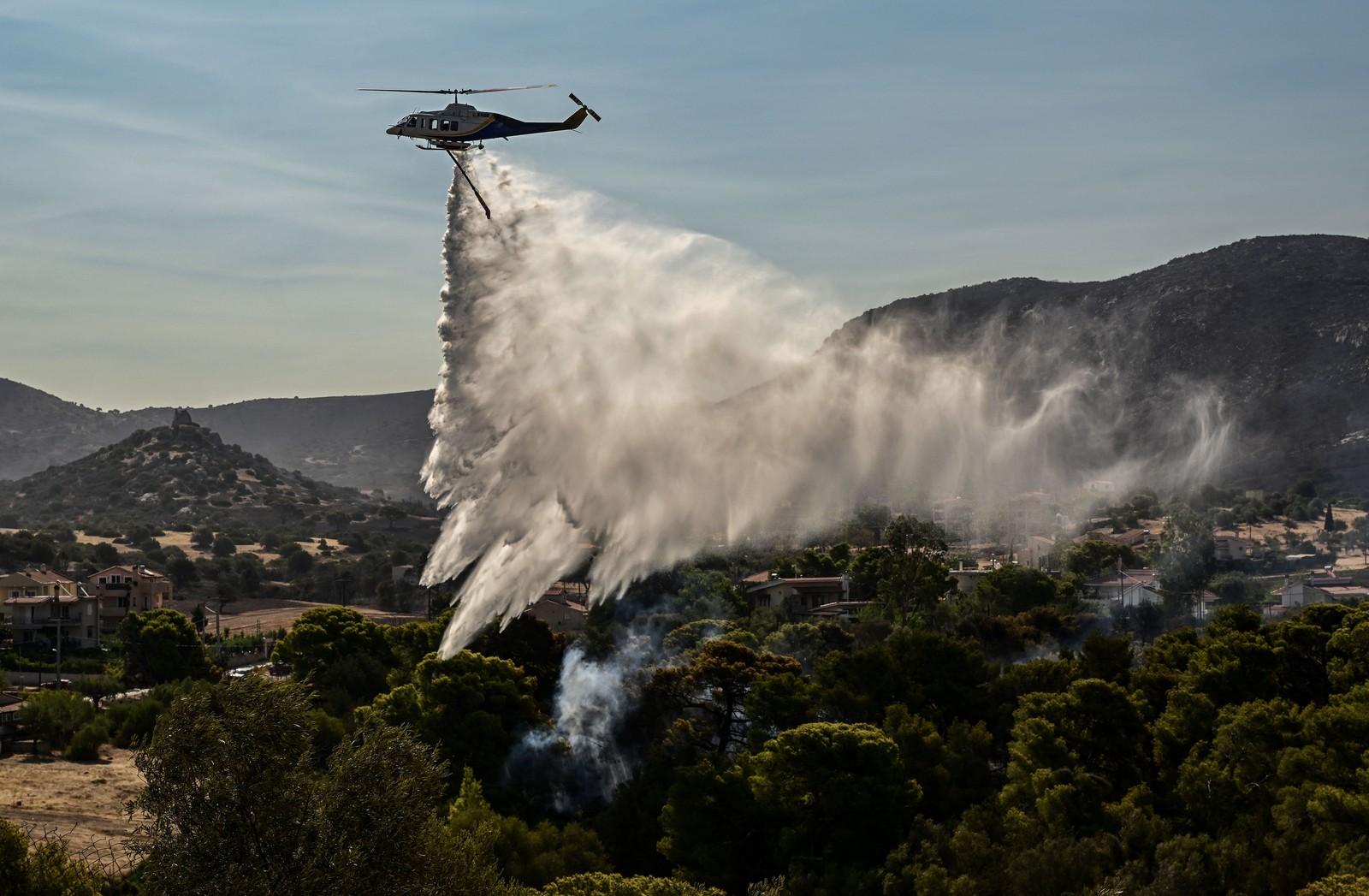 A firefighting helicopter drops water over a burned area.