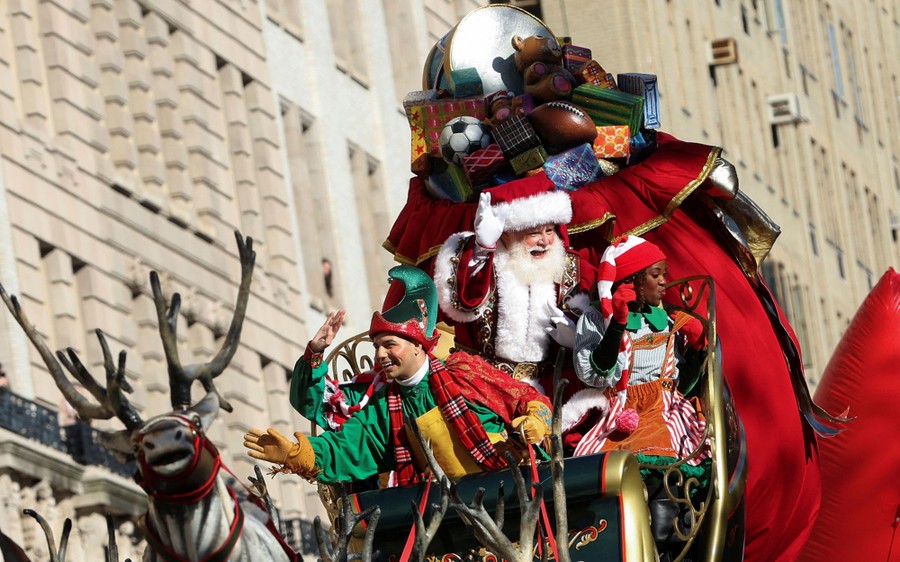 Santa and elf characters ride on a sleigh-shaped parade float.