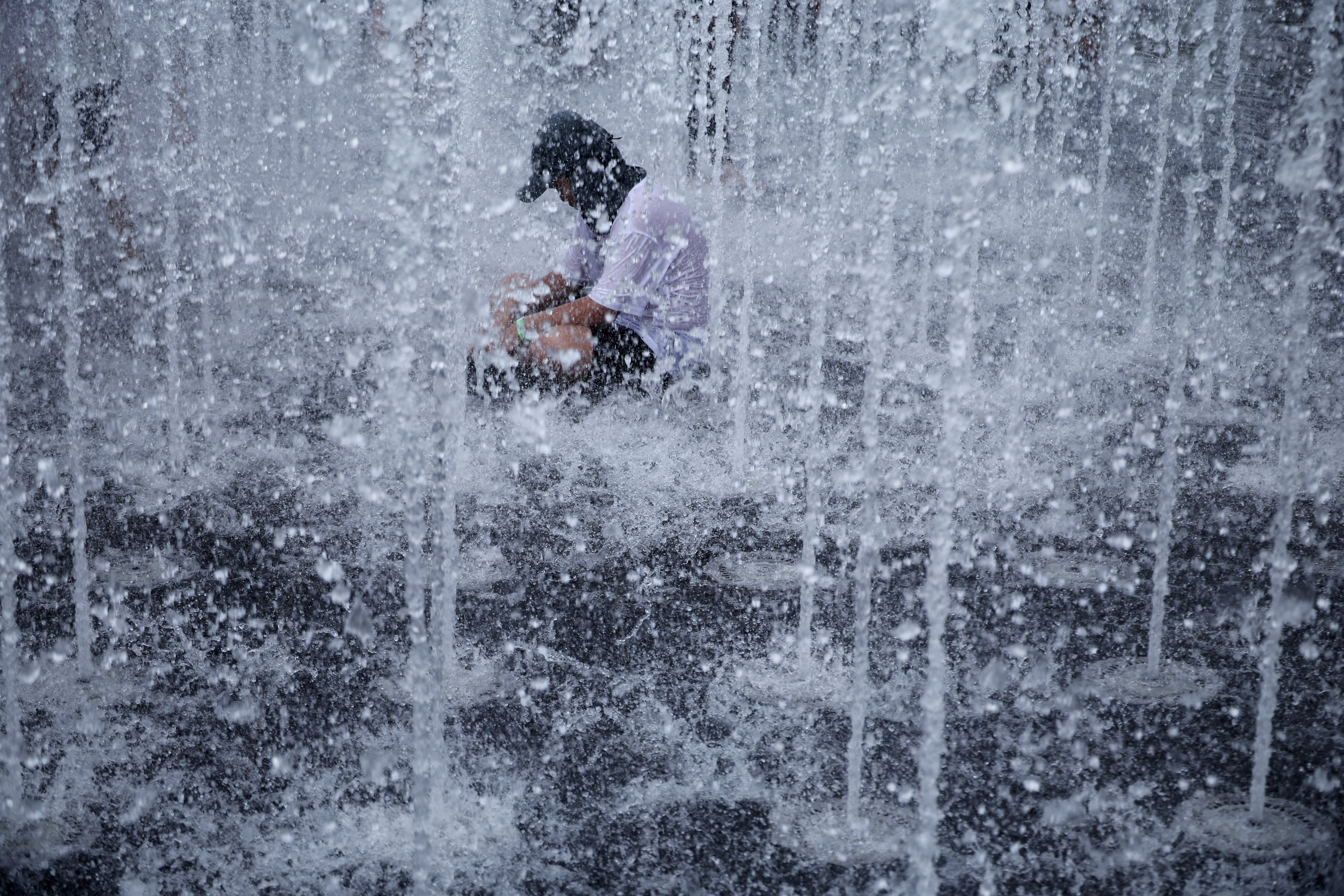 A boy cools down in a fountain, surrounded by jets of water.