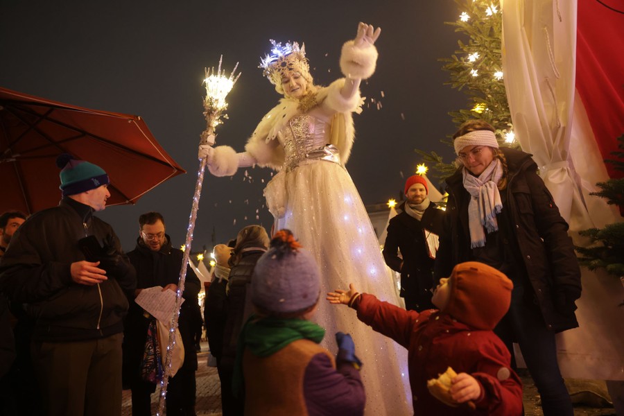 A costumed performer on stilts sprinkles snowflakes on children.