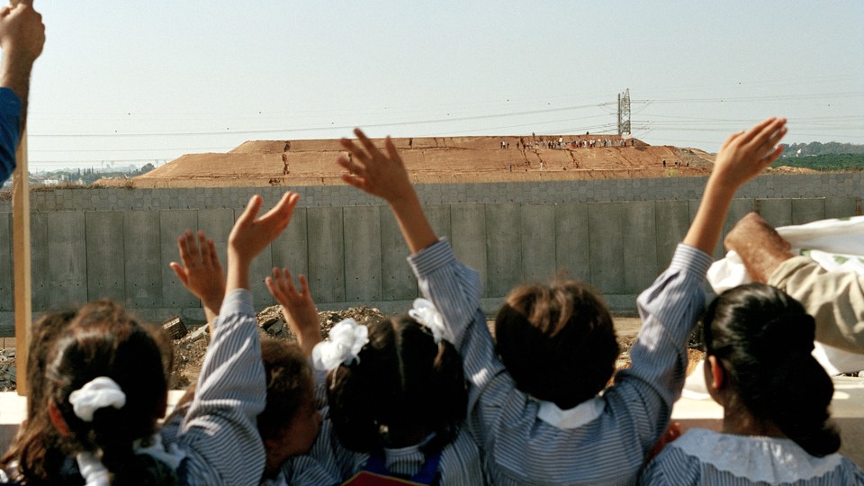 A photo of schoolgirls in the West Bank waving at Israelis who are on the other side of a wall
