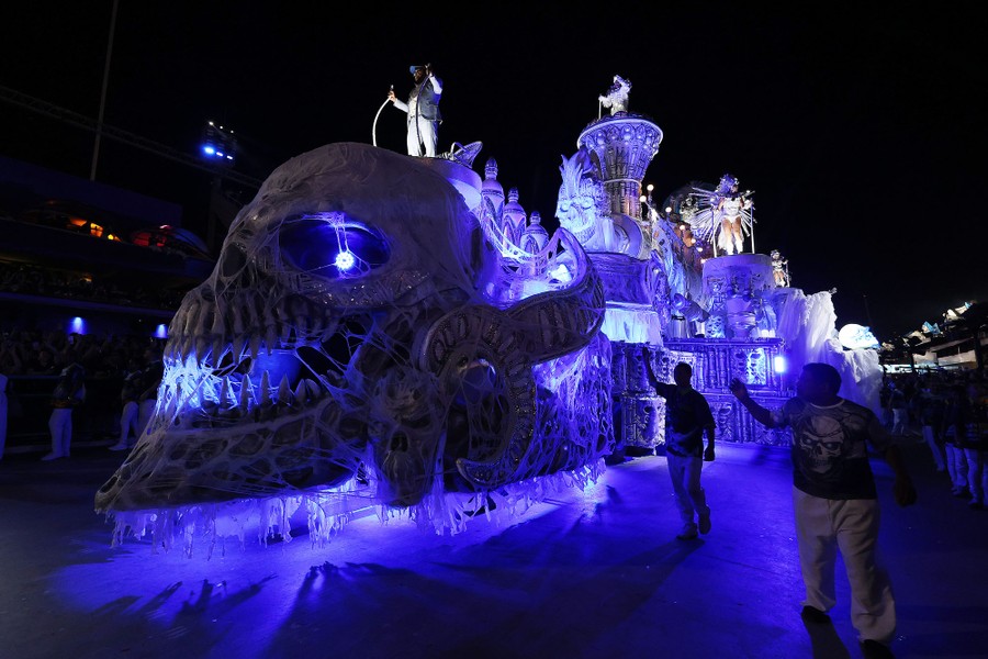 Performers ride on a large parade float whose front end is shaped like a frightening skull.