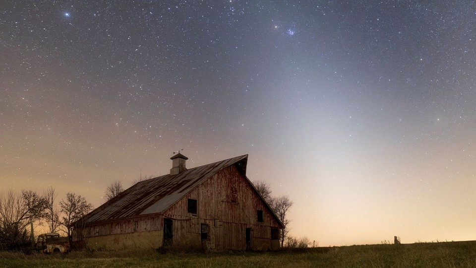 A photograph of an abandoned farm in rural Illinois at night, with the glow of zodiacal light overhead