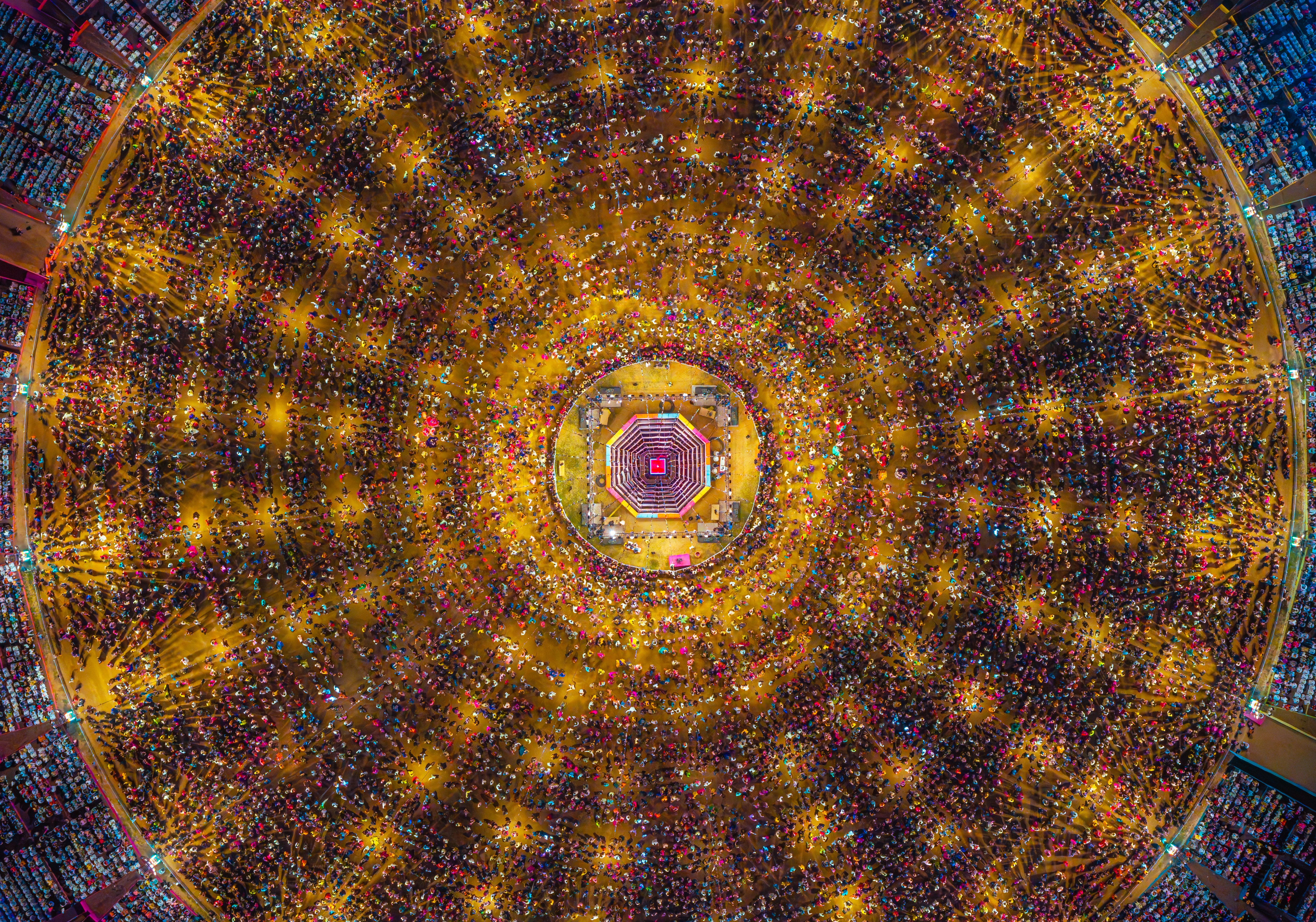 An aerial view of thousands of people dancing in concentric circles around a stage