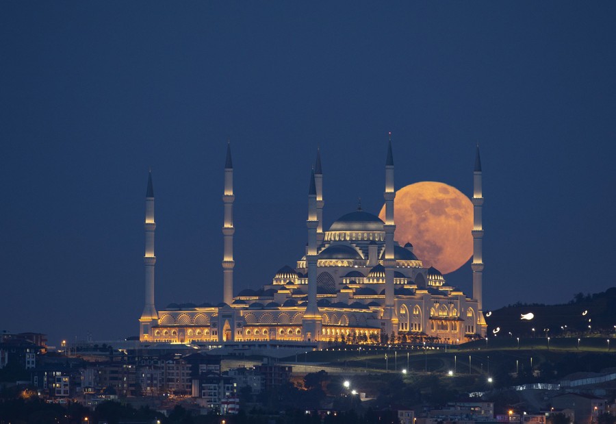 The full moon is seen behind a large mosque.