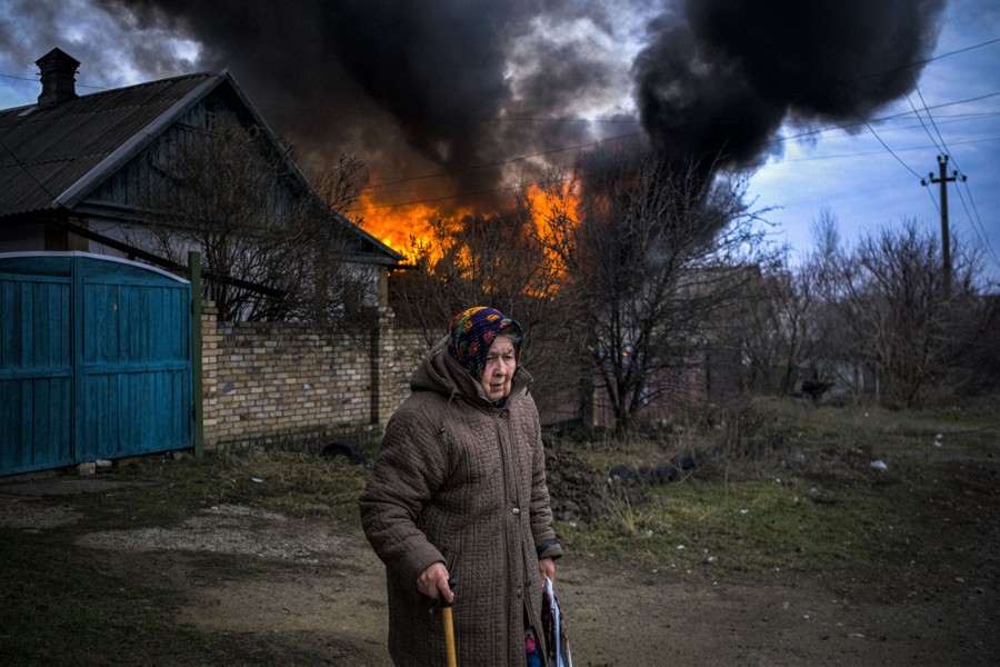 A woman stands near a burning building.