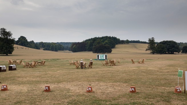 Two women sitting in chairs talking to each other in the midst of a wide open field at what looks like a concert venue